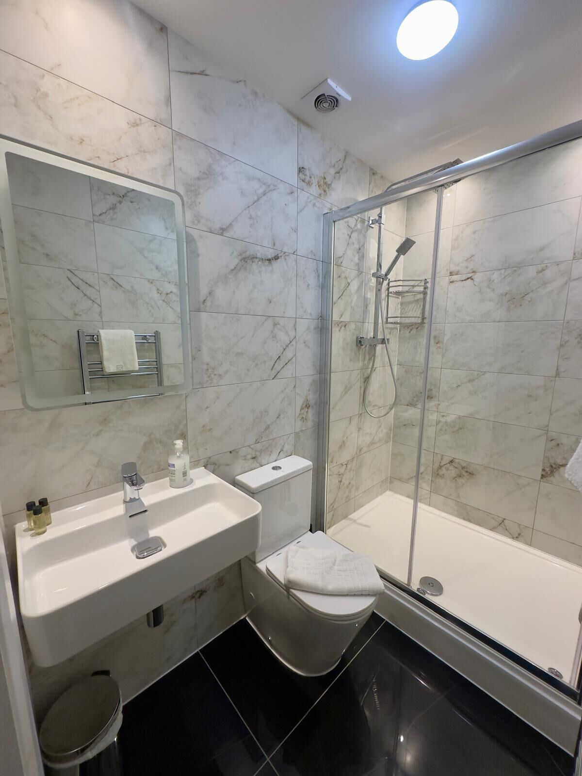 Un baño moderno con cabina de ducha de vidrio, un lavabo blanco con espejo y un inodoro.