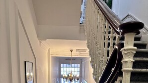 A grand staircase with white balustrades leading to a bright hallway with a chandelier. - Acacia Hotel (London)