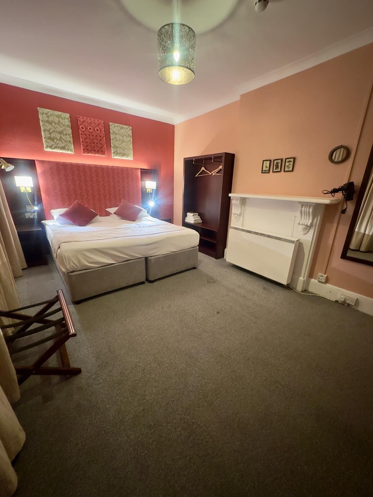 A bedroom with a bed, bedside tables, a wardrobe, a hanging coat rack, and a fireplace.