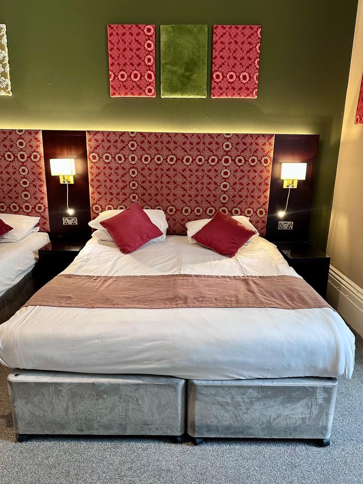 Un lit double avec deux oreillers rouges, un mur d’accent vert et deux lampes de chevet.