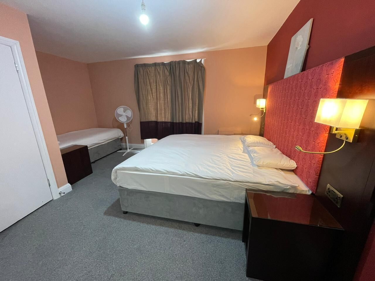 A hotel room with a bed, bedside table, lamp, and a small bench.