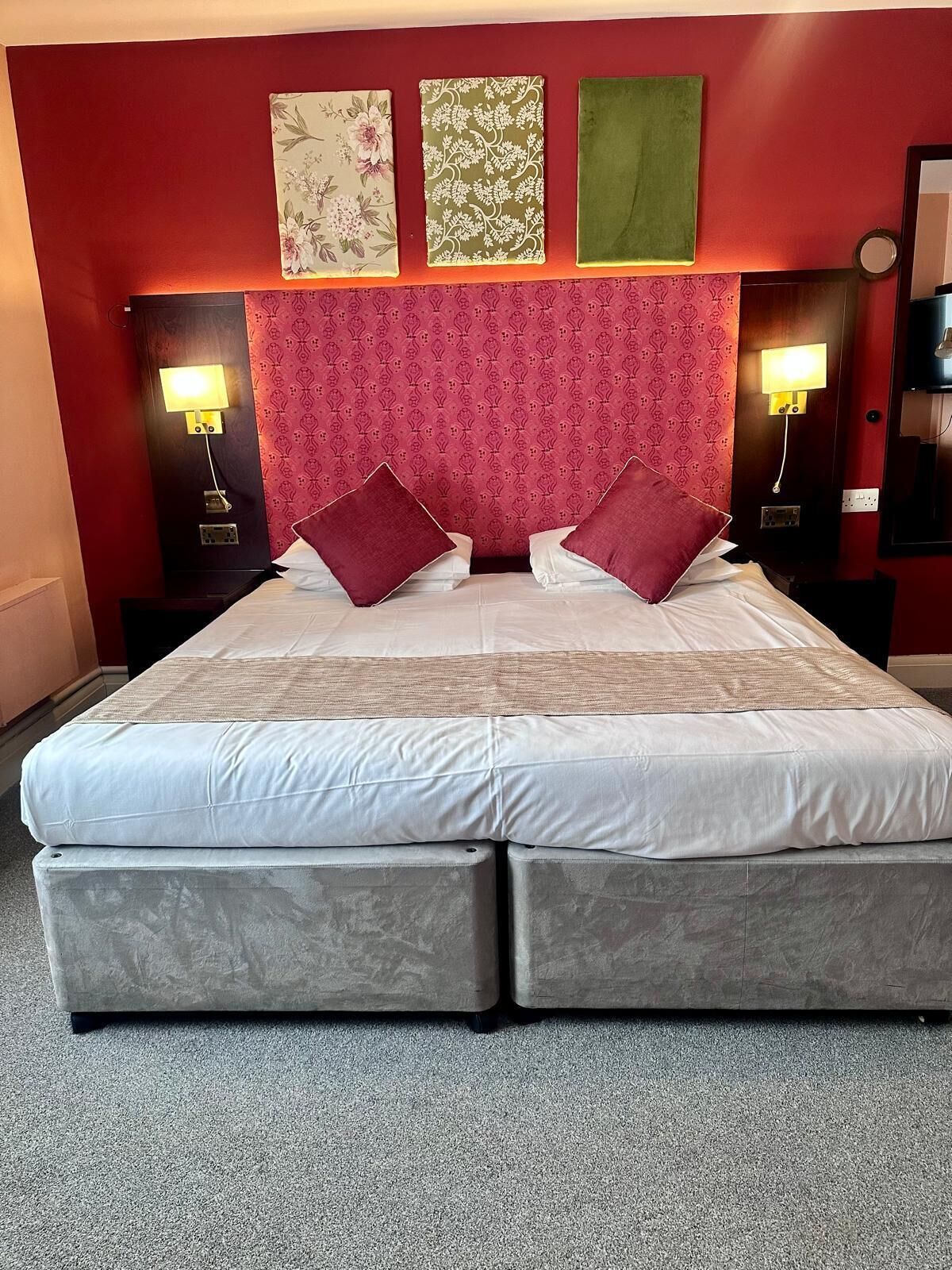 Habitación de hotel con una cama grande, dos mesitas de noche, un cabecero rojo estampado y tres obras de arte colgadas en la pared.