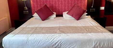 Habitación de hotel con una cama grande, dos mesitas de noche, un cabecero rojo estampado y tres obras de arte colgadas en la pared.