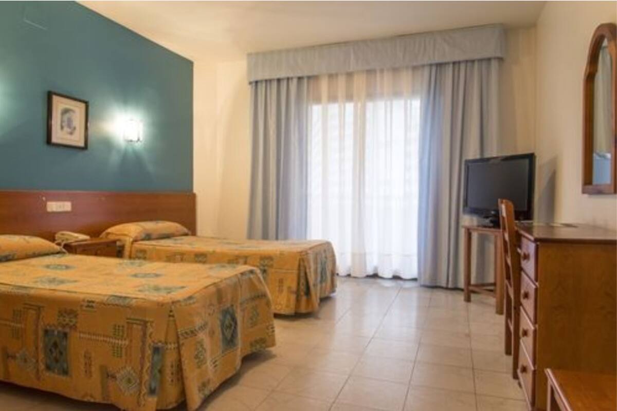 Habitación de hotel con dos camas, un televisor y un escritorio.