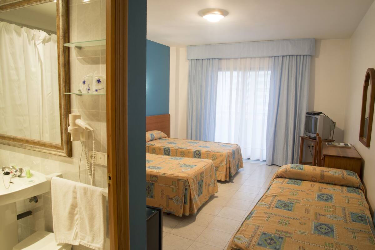 Habitación de hotel con dos camas, un baño con espejo y un televisor sobre un mueble de madera.