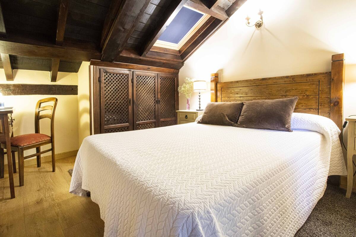 Un dormitorio con una cama grande, cabecera de madera, tragaluz, escritorio con silla y armario.