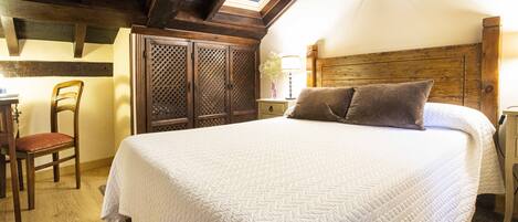Un dormitorio con una cama grande, cabecera de madera, tragaluz, escritorio con silla y armario.