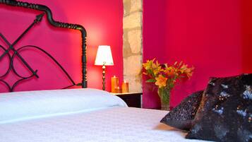 A bed with a white bedspread and black headboard, a bedside table with a lamp, a vase with flowers, and a stone wall.