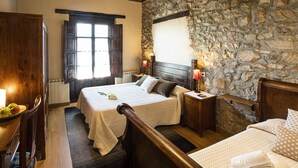 Un dormitorio con dos camas, una pared de piedra, muebles de madera y una ventana con contraventanas.