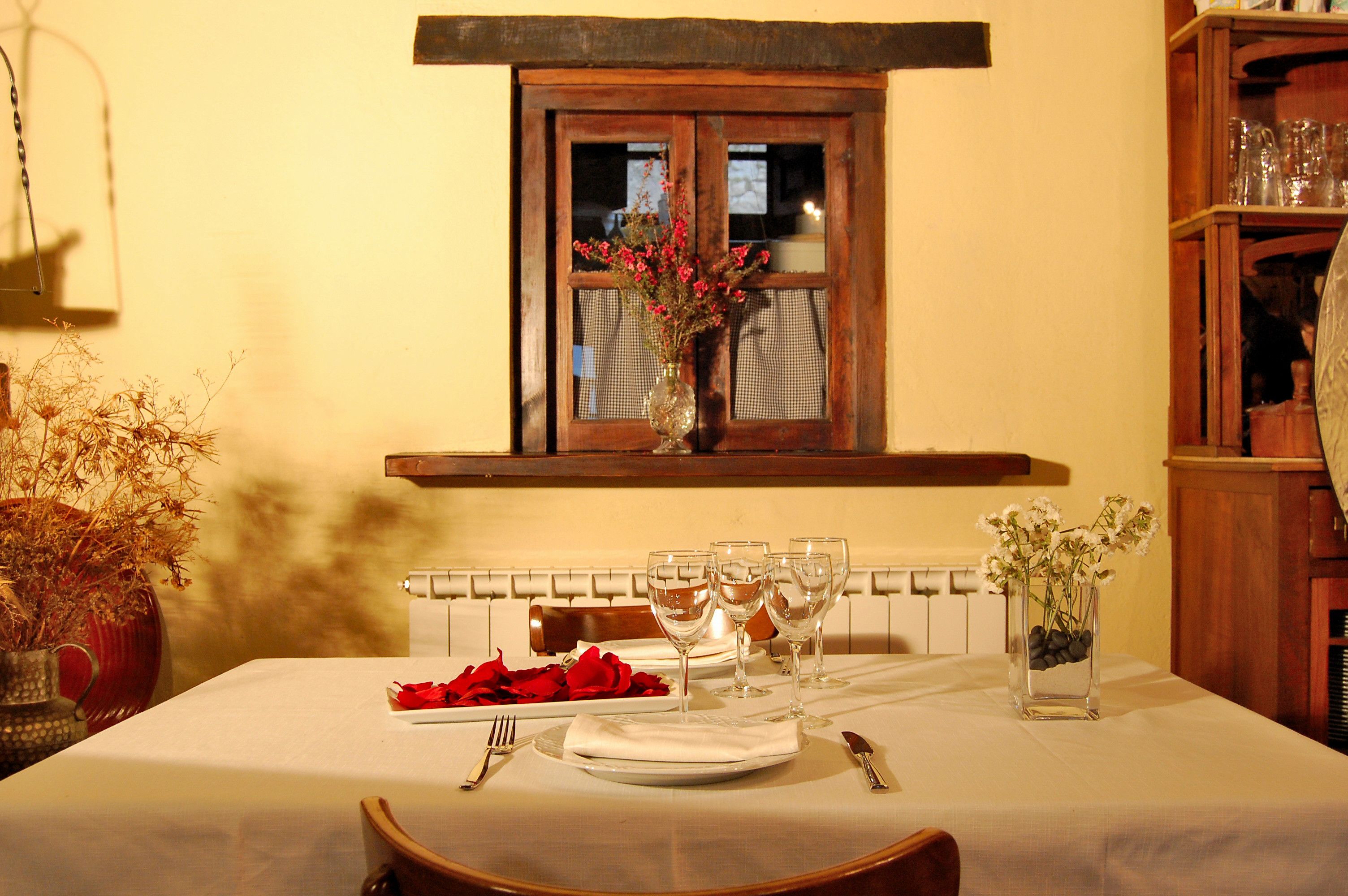 A dining table set with plates, glasses, and a vase of flowers.