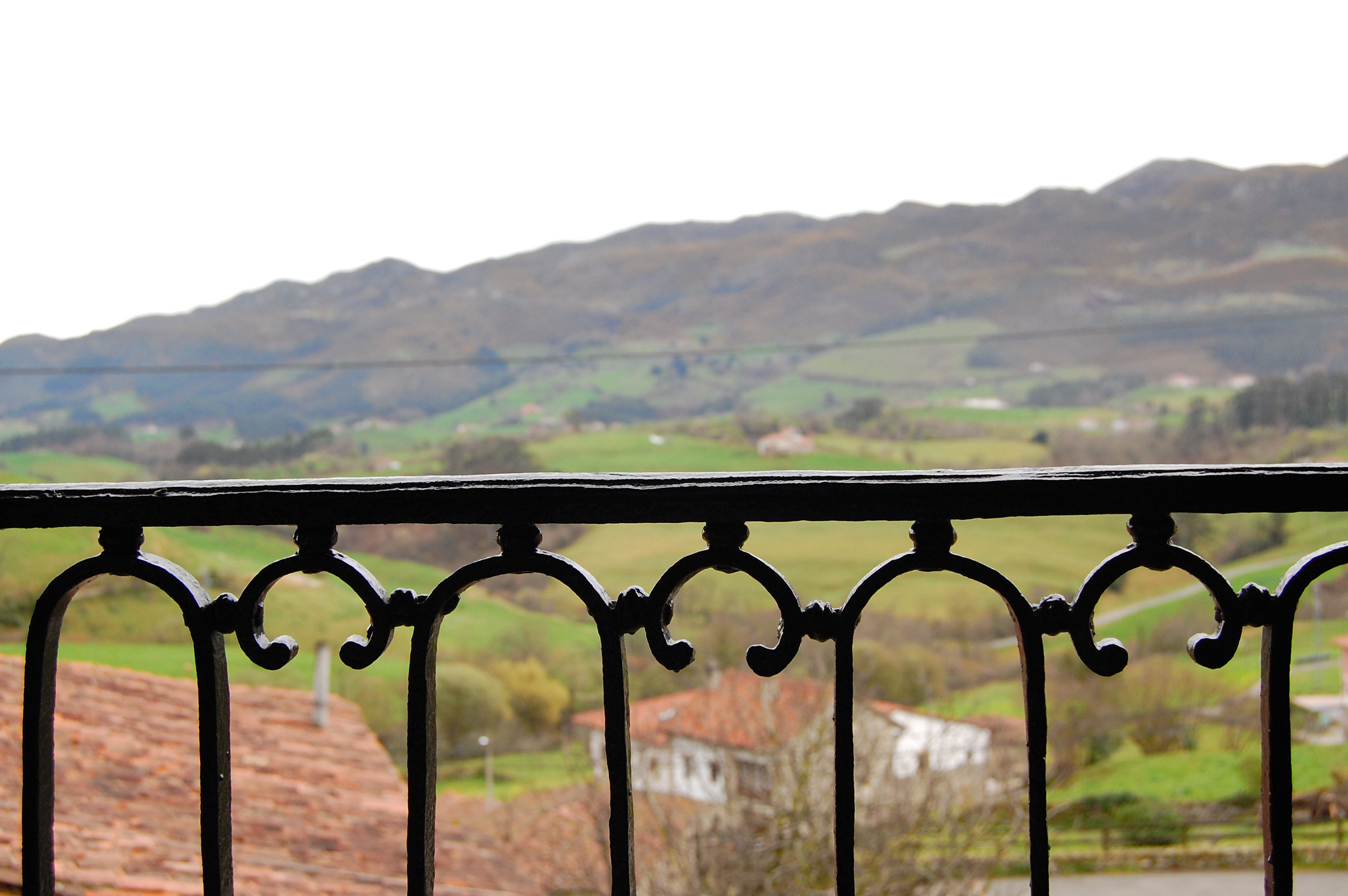 A balcony with a wrought iron railing overlooking a rural landscape with rolling hills and scattered buildings.
