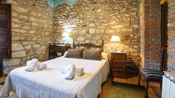 A stone-walled bedroom with a bed, two bedside tables, a wooden chair, and a nightstand.