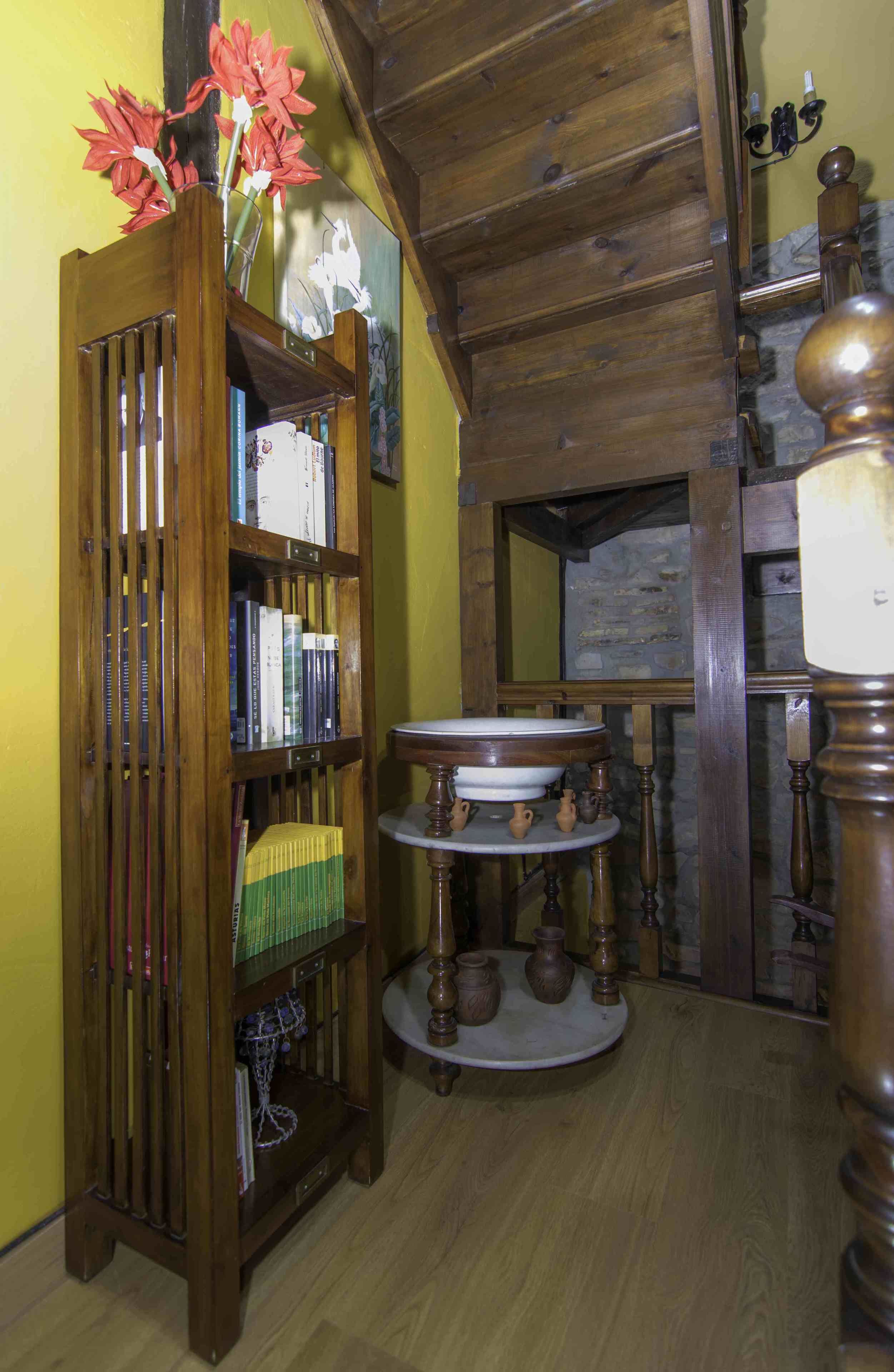Una habitación con una estantería de madera, una mesa redonda con cerámica y un espejo en la pared.