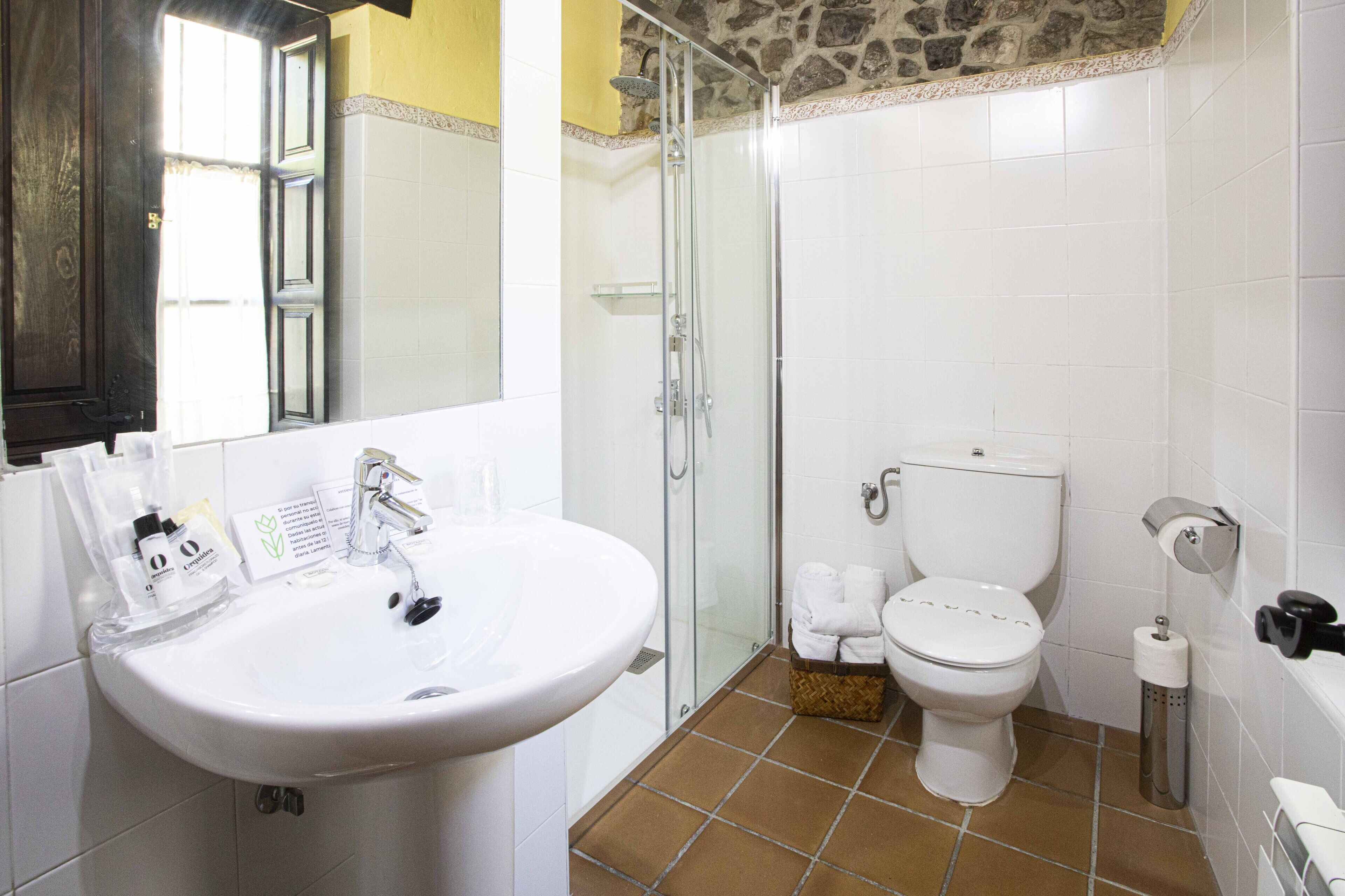 A bathroom with a white sink, a glass shower enclosure, a white toilet, and a tiled floor.