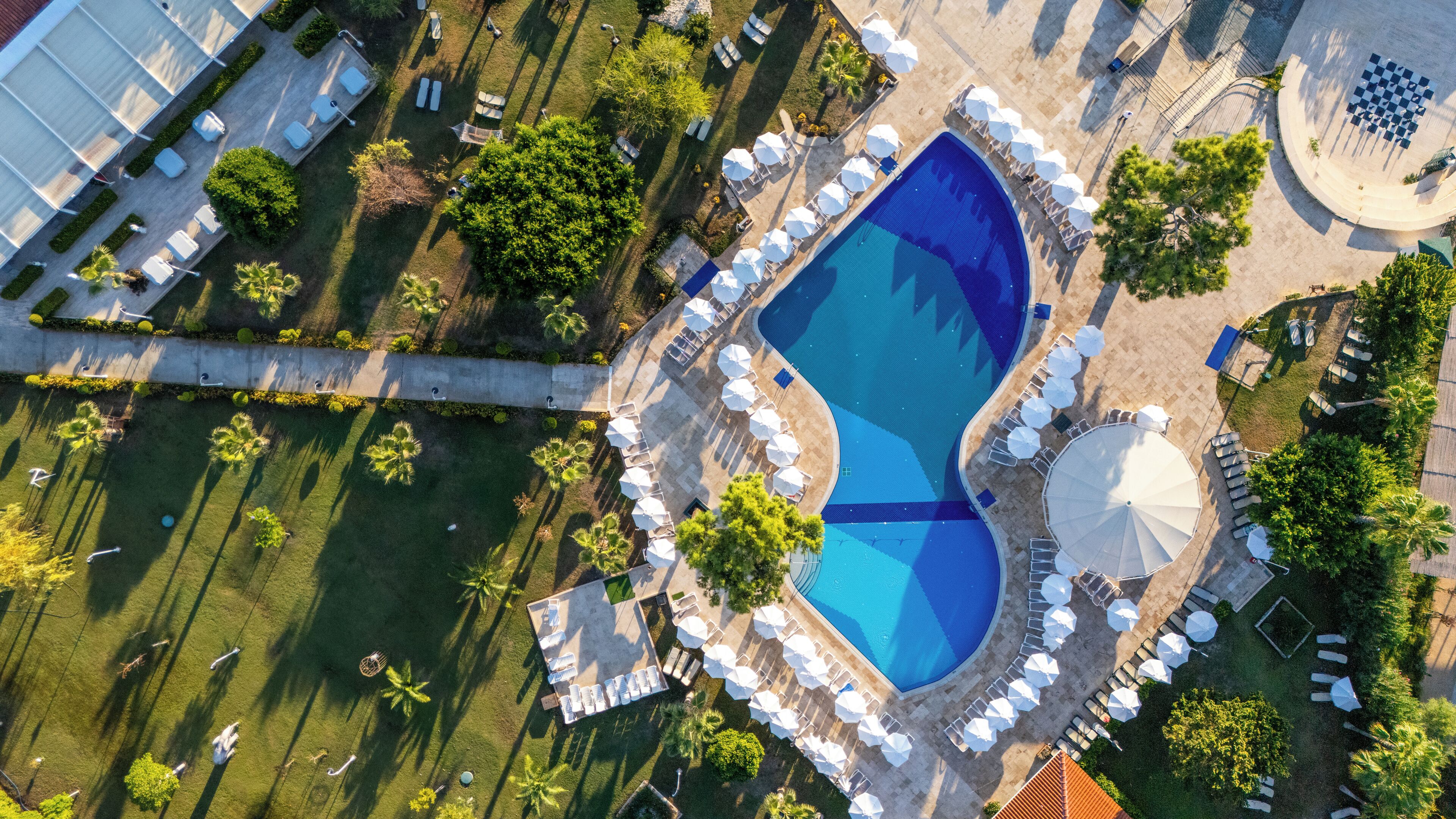 An aerial view of a resort with a large pool, sun loungers, and palm trees.