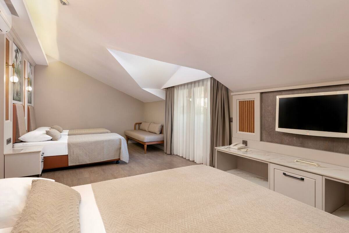 A modern hotel room with a large bed, a desk, a flat-screen TV, and a window with curtains.