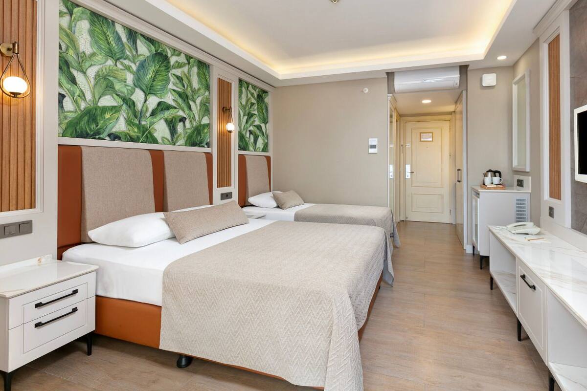 A hotel room with two beds, a TV, a bathroom, and a large window with a tropical wallpaper.