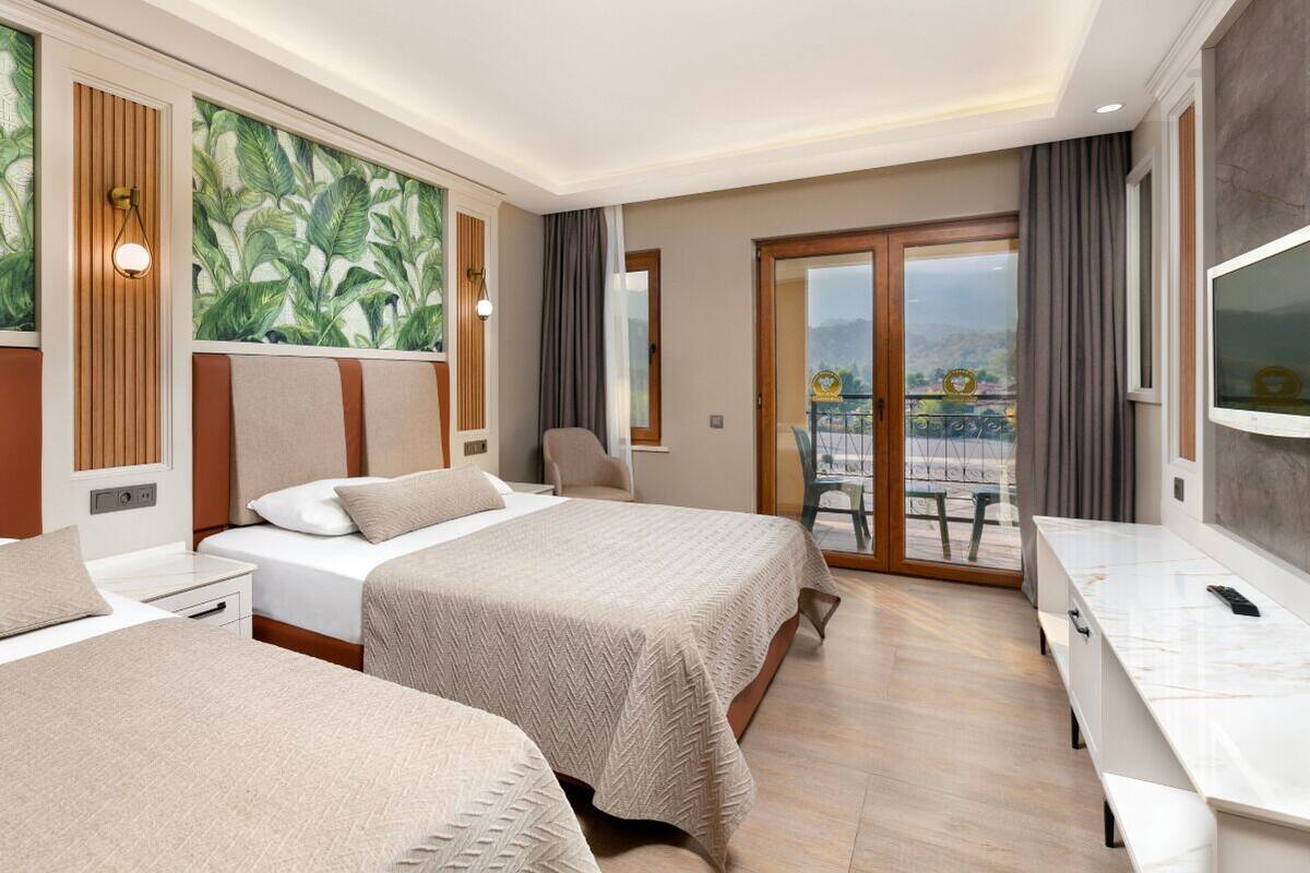 A hotel room with two beds, a desk, a TV, and a balcony with a view.