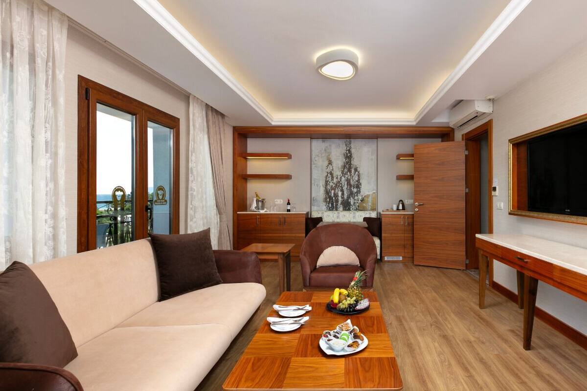 A hotel room with a sofa, dining table, TV, and a view of the outdoors.