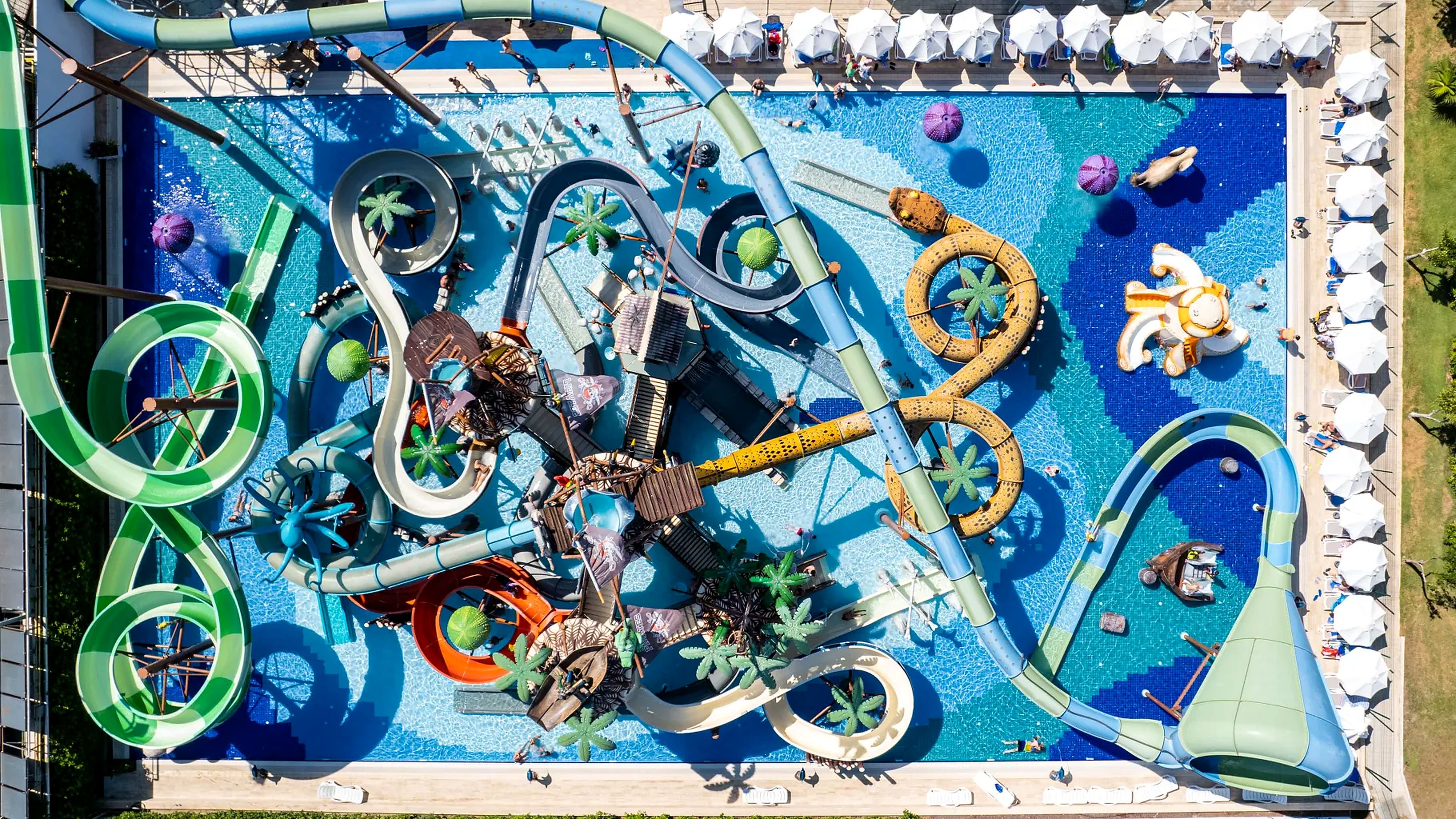 A pool with multiple water slides and rings, surrounded by lounge chairs and umbrellas.