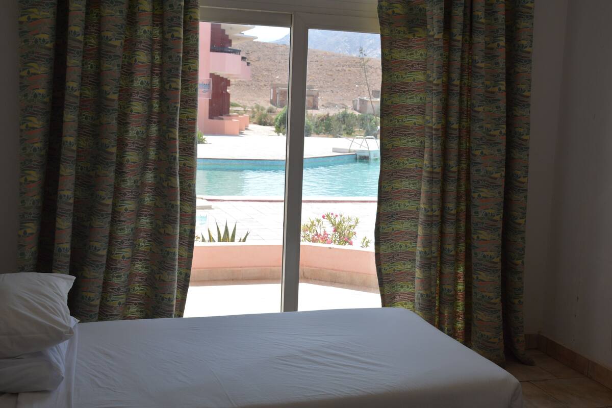 Une chambre d’hôtel avec un lit, une vue sur une piscine et des rideaux à motifs.