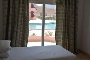 Ein Hotelzimmer mit einem Bett, Blick auf einen Swimmingpool und gemusterten Vorhängen.
