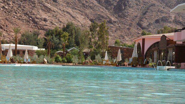 Un espace piscine doté de chaises longues et de parasols, entouré d’un paysage montagneux.