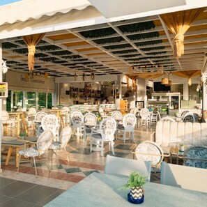 An outdoor café with white chairs and tables, a bar area, and a view of the street. - Panorama (Skiathos)