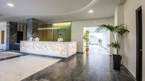 A modern reception area with a marble counter, a receptionist, and potted plants. - Exotica Hotel (Zakynthos)