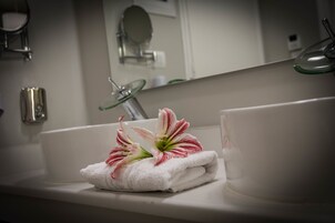 Un bagno con un lavandino bianco, un erogatore di sapone in vetro e un asciugamano con fiori.