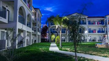 Un hotel de varios pisos con un patio central, mobiliario exterior y un césped cuidado.