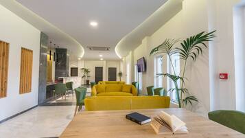 Un moderno vestíbulo de hotel con un mostrador de recepción de madera, un sofá amarillo, sillas verdes y plantas en macetas.
