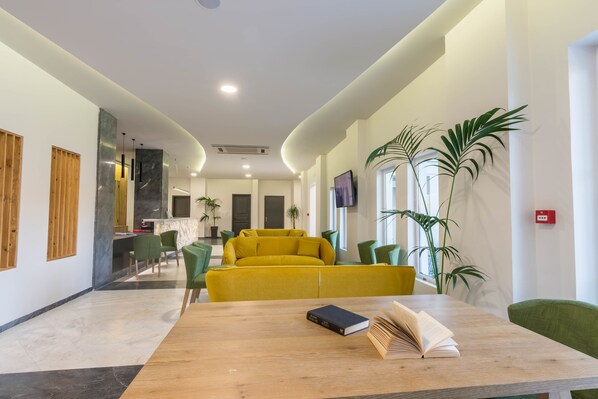 A modern hotel lobby with a wooden reception desk, a yellow sofa, green chairs, and potted plants. - Exotica Hotel (Zakynthos)