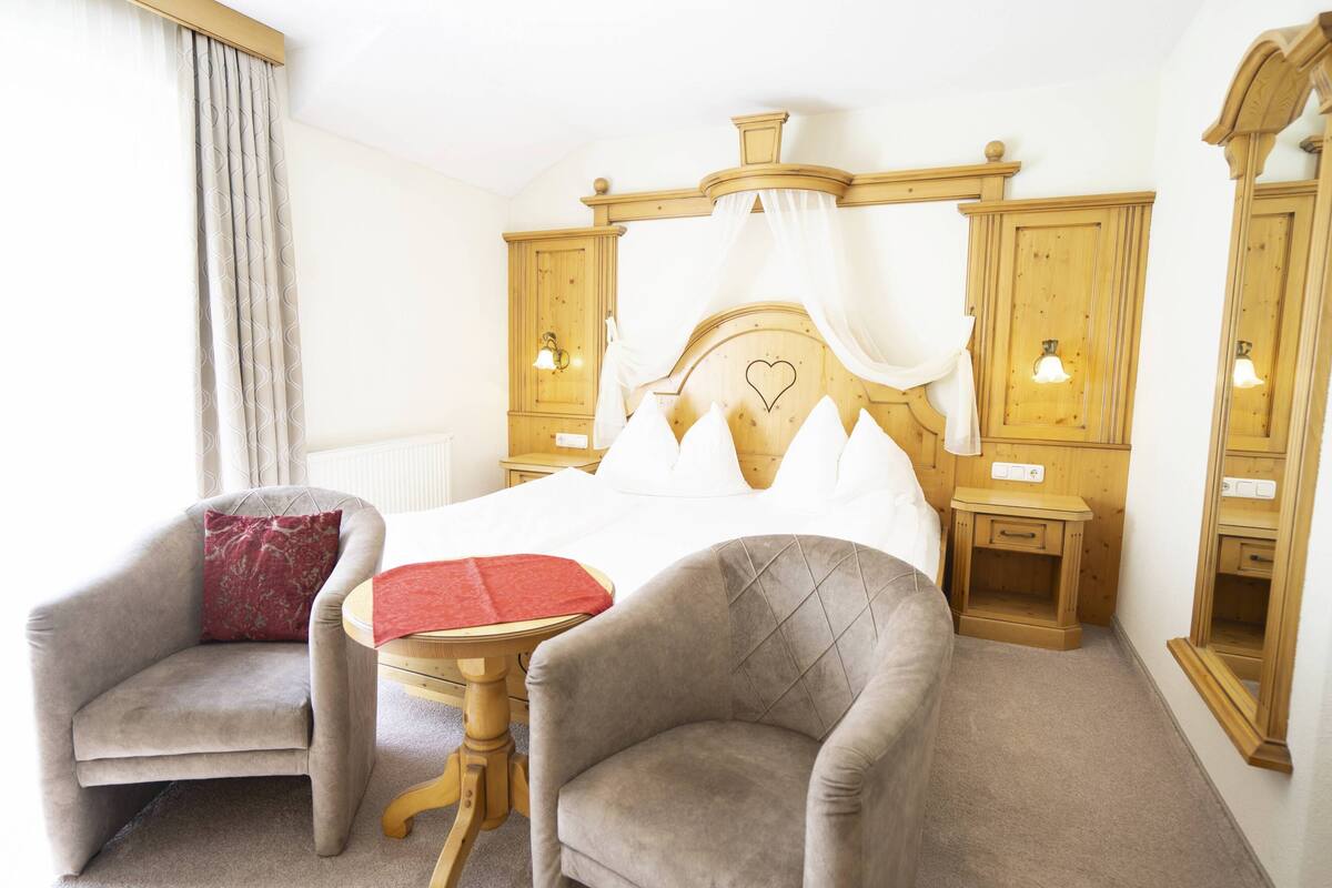 A hotel room with a bed, two armchairs, a small table, wooden cabinets, and a nightstand.