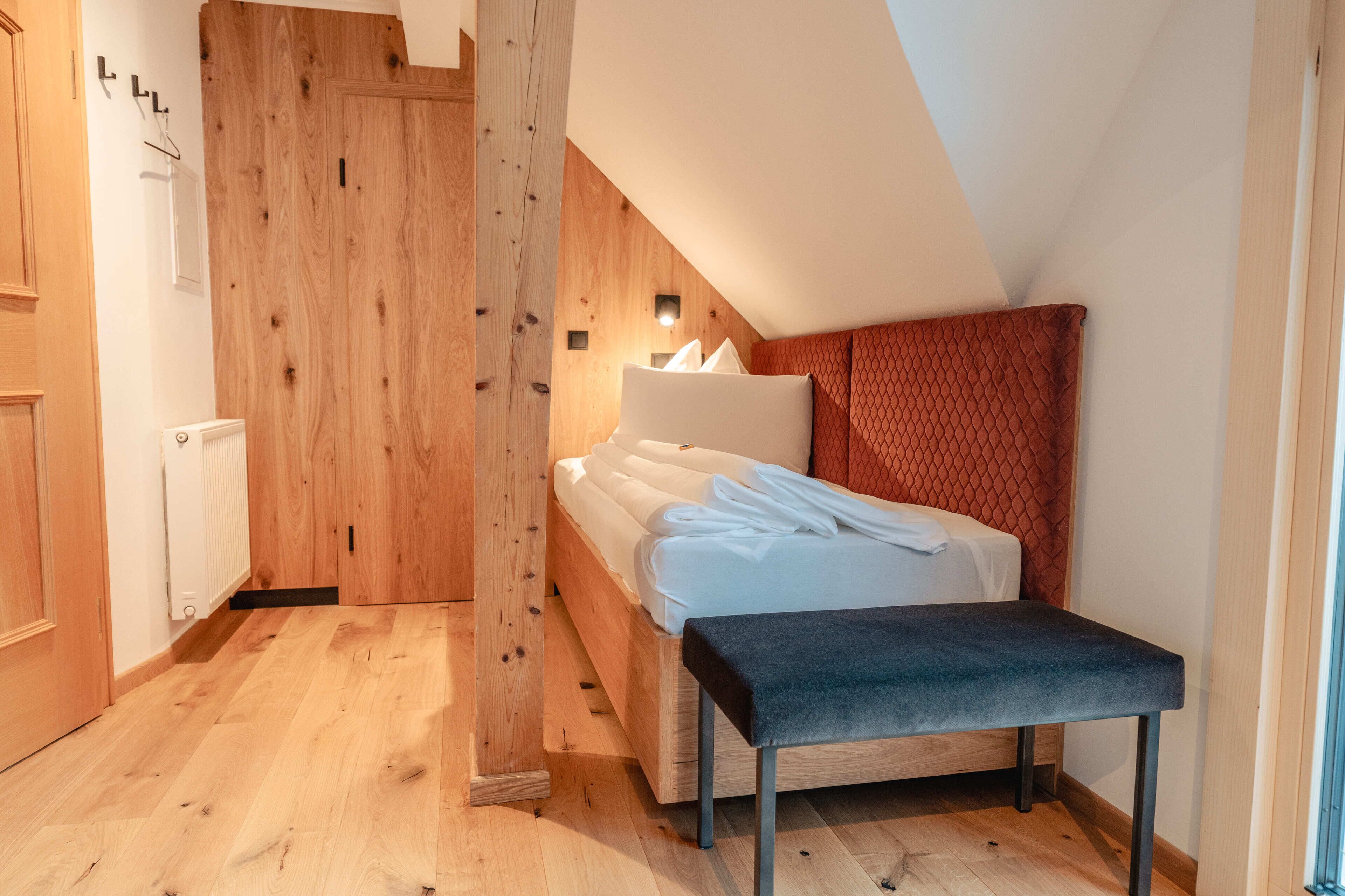 Ein Schlafzimmer mit Holzboden, einem Bett mit weißer Bettwäsche, einer Bank und einem roten, gemusterten Kopfteil.