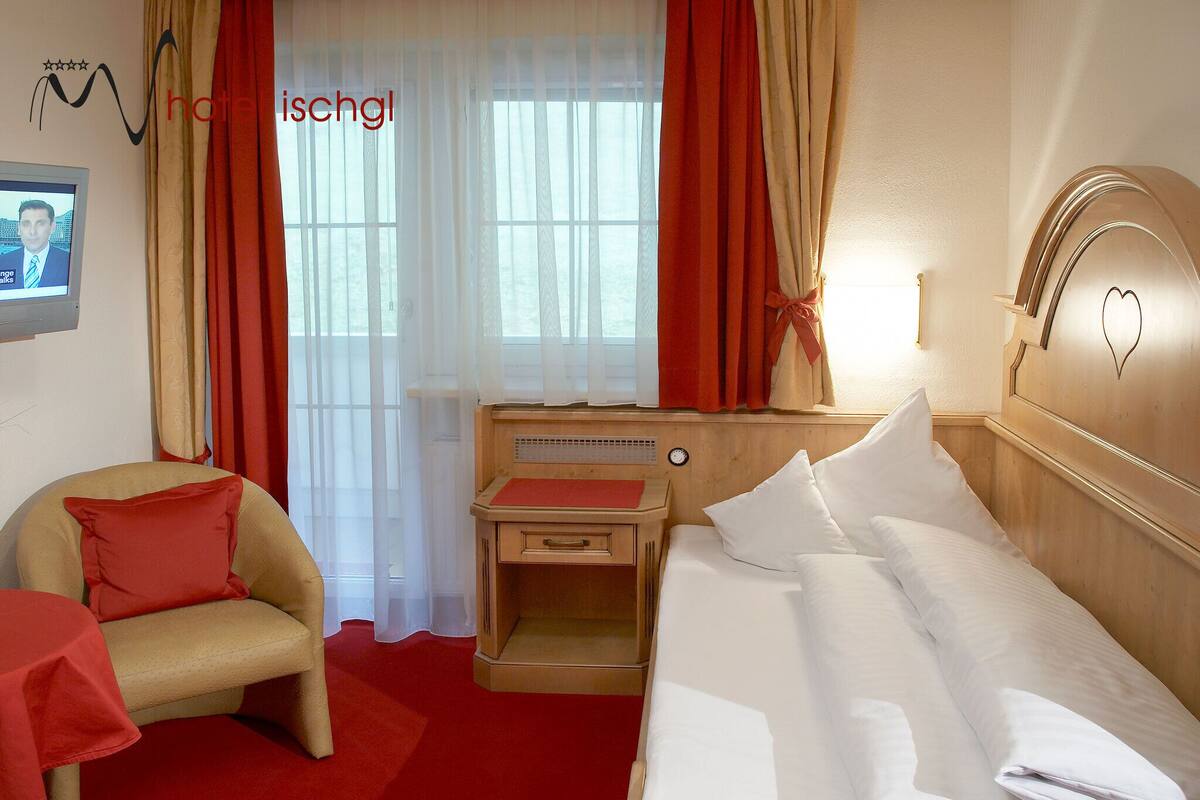 A hotel room with a bed, a chair, a nightstand, and a window with curtains.