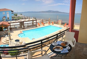 A poolside area with a view of the sea, a dining table with food, and lounge chairs. - Gera Bay Studios and Apartments (Lesvos)