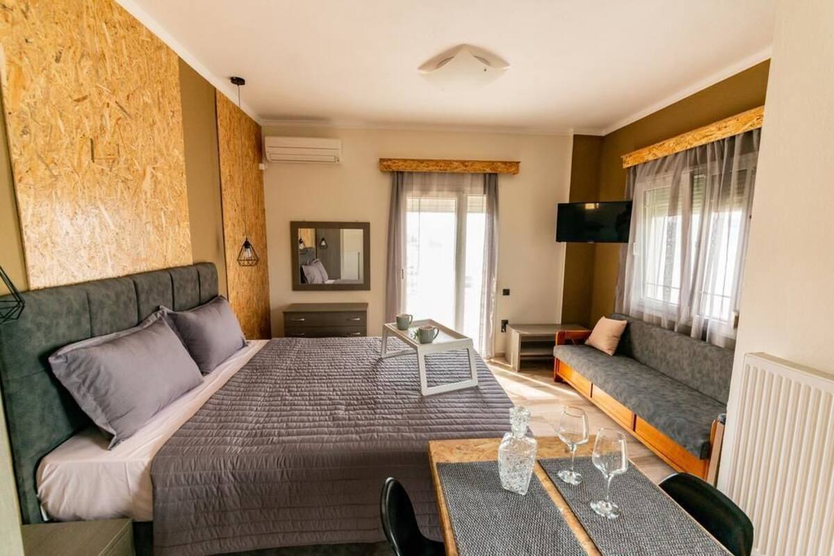 A hotel room with a bed, a sofa, a TV, a table with glasses, and a window with curtains.
