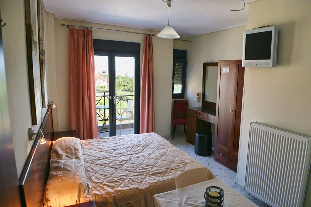 A hotel room with a bed, a small table, a radiator, a TV, and a balcony with a chair.