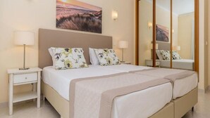 A double bed with floral pillows, a bedside table with a lamp, and a large mirror. - Vila Marachique (Portimão)