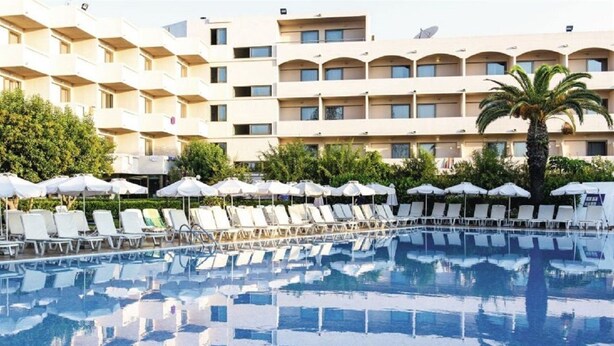 A swimming pool with sun loungers and umbrellas, surrounded by a multi-story hotel building. - Ialyssos Bay (Rhodes)