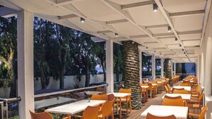 An outdoor dining area with tables and chairs, large windows, and a view of trees. - Ialyssos Bay (Rhodes)