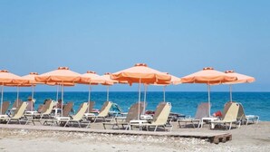 A beach with rows of sun loungers and orange umbrellas. - Ialyssos Bay (Rhodes)