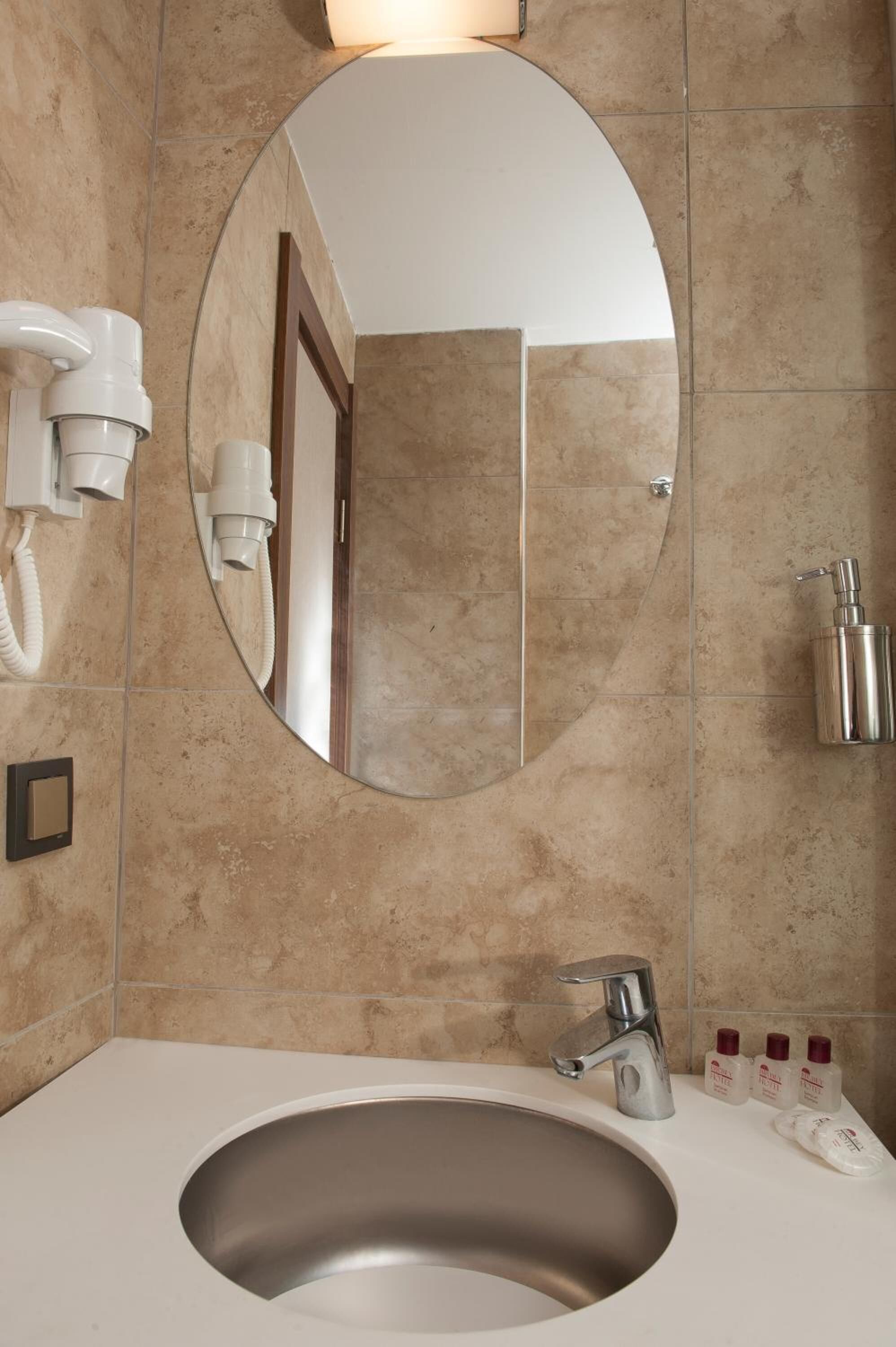 Un baño con lavamanos, espejo y secador de pelo fijado a la pared.