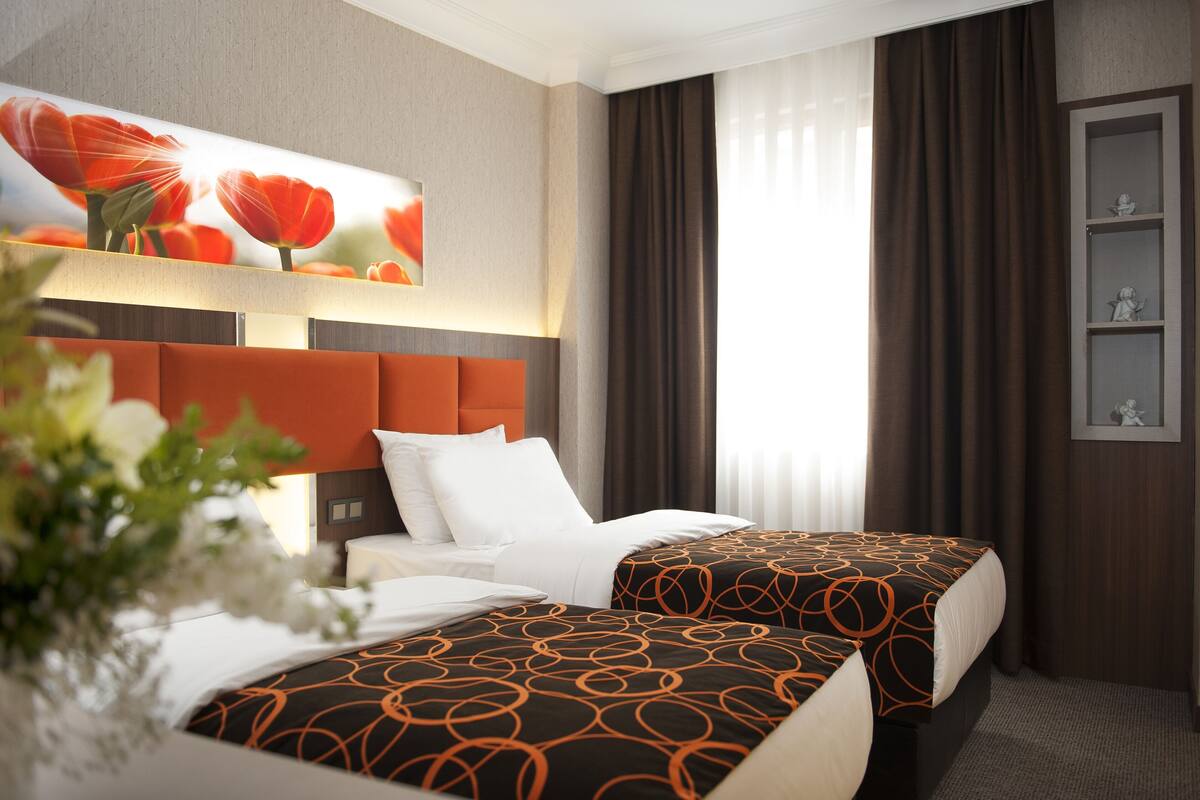 A hotel room with two beds, a large painting of flowers, a vase with flowers, and a shelf with decorative items.