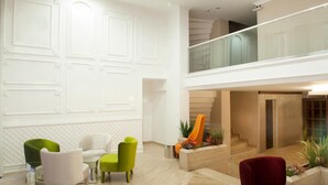 Un vestíbulo amplio con techo alto, una escalera y una zona de estar con sillas modernas.