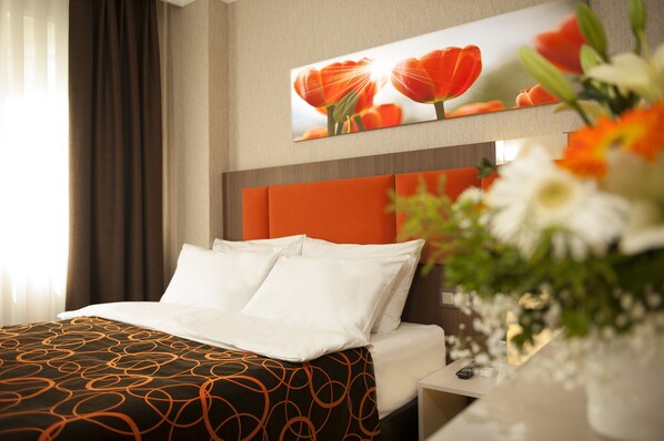 A hotel room with a bed, a nightstand, a vase with flowers, and a painting of flowers on the wall. - Hotel Birbey (Istanbul)