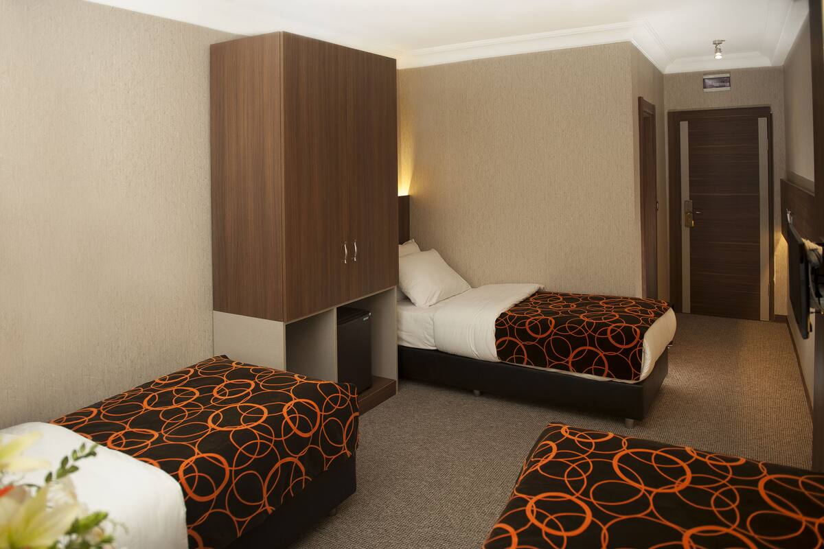 A hotel room with two single beds, a wardrobe, a small trash bin, and a nightstand.