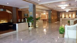 A spacious lobby with a reception desk, a seating area, and a staircase leading to upper floors. - The Ariston (Bangkok)