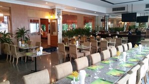 A restaurant with multiple dining tables and chairs, some with flower centerpieces. - The Ariston (Bangkok)